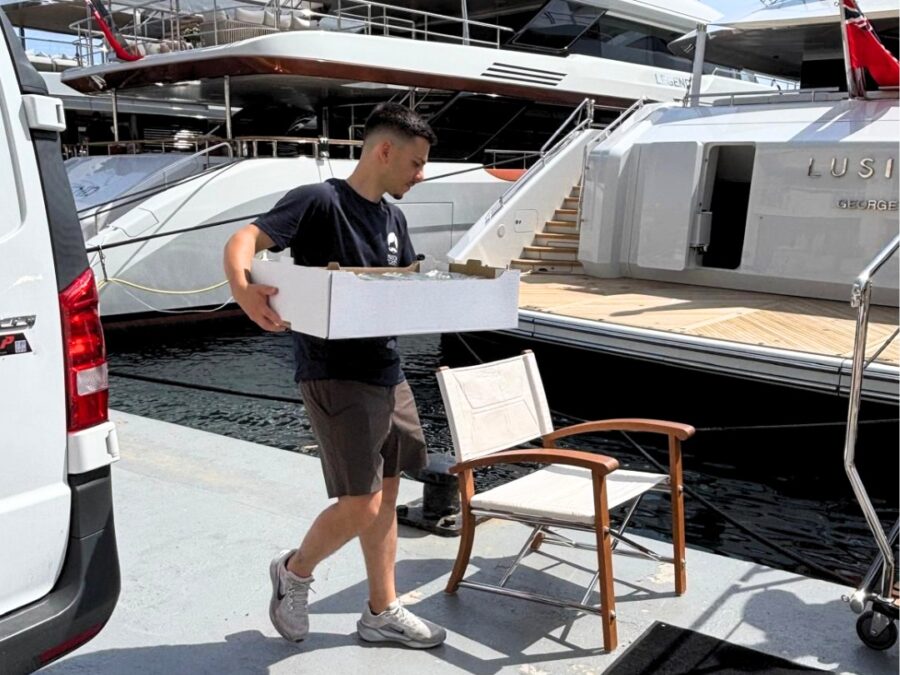 A Maison del Gusto team member carrying a provisioning box beside yachts in Monaco